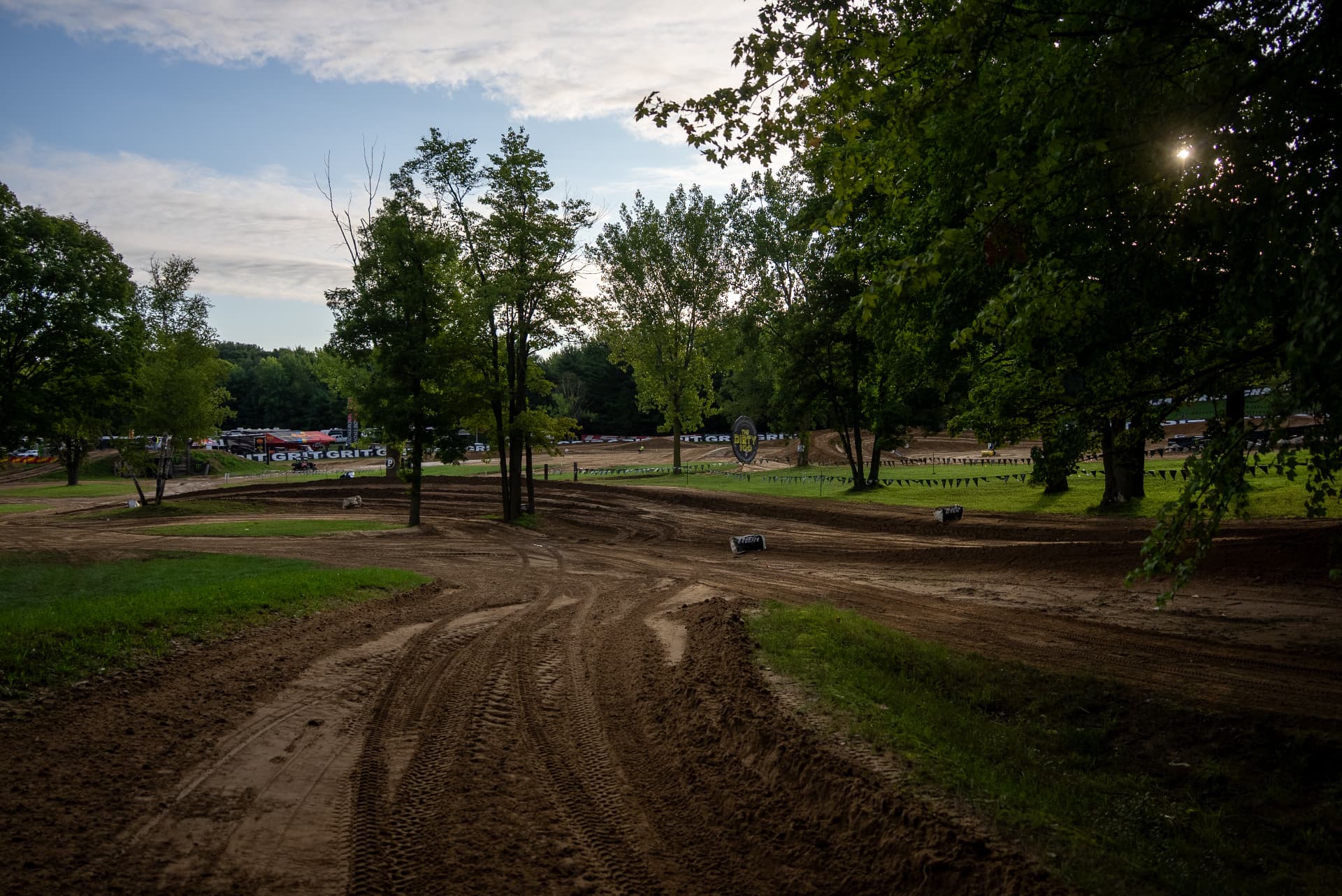 A motocross track winding through trees and grass, late afternoon light.